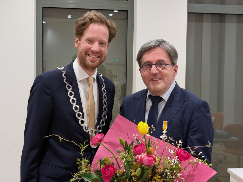 Burgemeester overhandigt een bos bloemen aan Jan Dijkstra